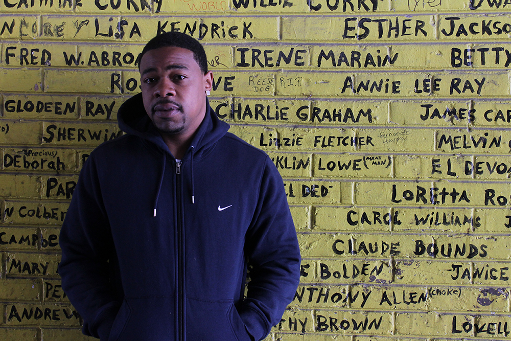 A resident of Altgeld Gardens, a public housing complex on Chicago's far South Side, stands in front of a memorial wall. The wall contains handwritten names of people who have died in the complex since its earliest days. Photo credit: Robyn Murray/MEDILL